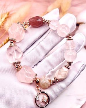 A gloved hand holding a delicate crystal bracelet with pink and translucent gemstones, along with si