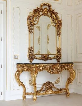 a gold console table with a mirror on the wall