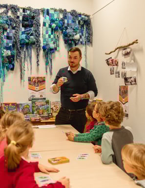 Animateur expliquant un jeu à un groupe d’enfants dans un espace coloré et ludique.
