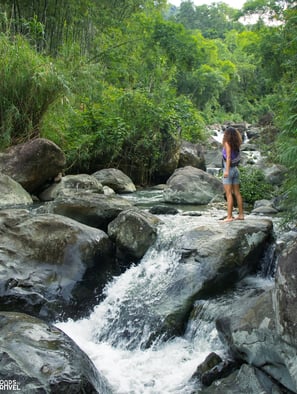 Woman standing on rock as she looks ahead, by a mountain cascade in Pu Luong Vietnam