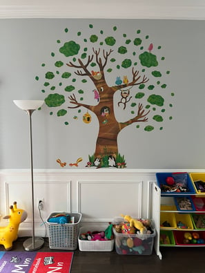 Photo of daycare room where children play. Large tree sticker on wall.