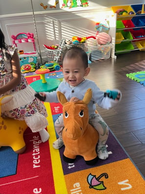 Photo of young child laughing while playing on a toy horse.