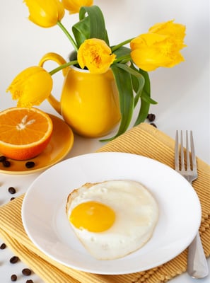 Fried egg, juicy orange, bouquet of yellow tulips, yellow napkin and fork