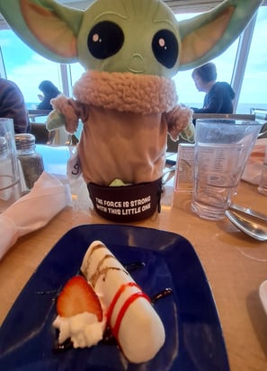 Little green companion on table in front of plate with Strawberry blintz