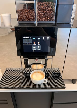 Thermoplan Black&White 4c espresso machine preparing a cappuccino with a touchscreen interface.
