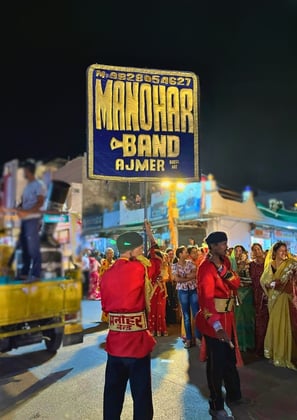 The Manohar Brass Band signboard banner illuminated at night, adding a vibrant touch to the surroundings.