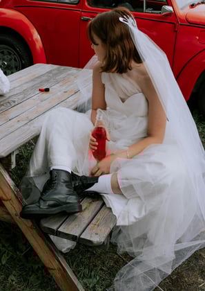 a young women on her wedding day, dressed in funky doctor martins witha red bettle car behind her