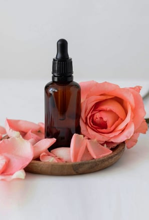 un flacon d'huiles essentielles avec une rose sur un bol en bois
