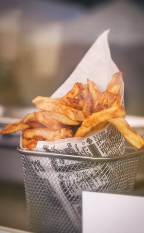 Golden fries wrapped in paper, gently placed in a sleek sieve, capturing the essence of a restaurant