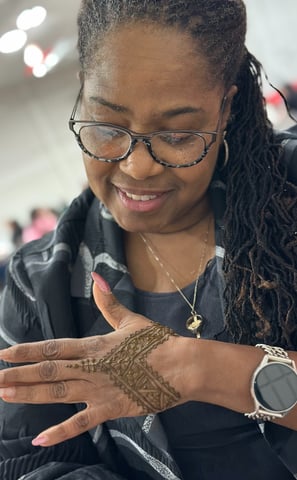 Black woman with glasses looks at the henna on her hand and smiles