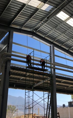 Trabajadores instalando tuberías aéreas en el techo de una nave industrial.