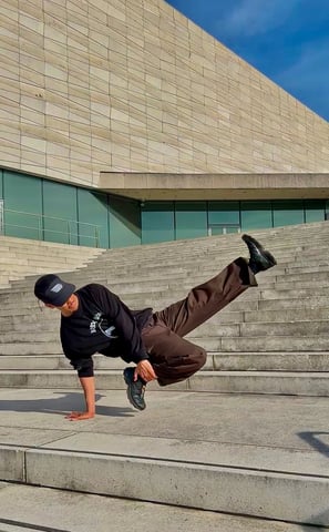 YoYo performing a breakdance move in front of concrete building.