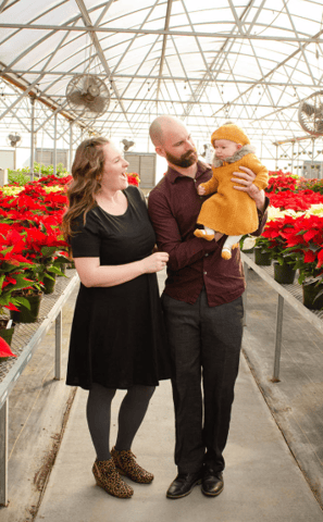 a man and woman holding a baby in a greenhouse