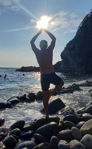 a man performing yoga on rocks in the sea