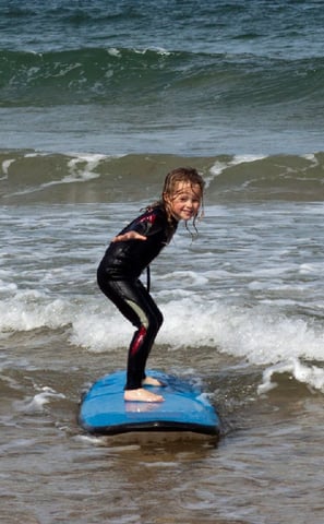 A young girl taking a surf lesson riding a blue surfboard on the water
