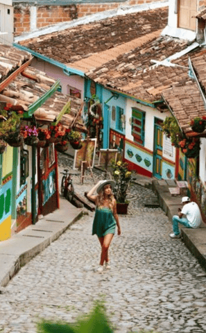 Una Mujer paseando por una calle tradicional de Guatapé, con sus casas adornadas con zocalos