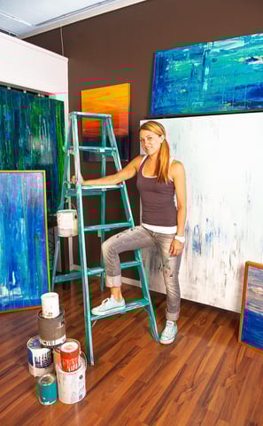 a portrait of a woman in a brown tank top and jeans standing on a ladder