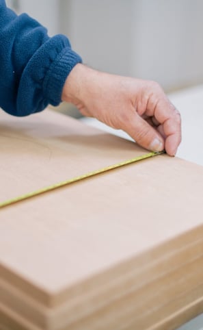 Mano midiendo tabla de madera con cinta métrica.
