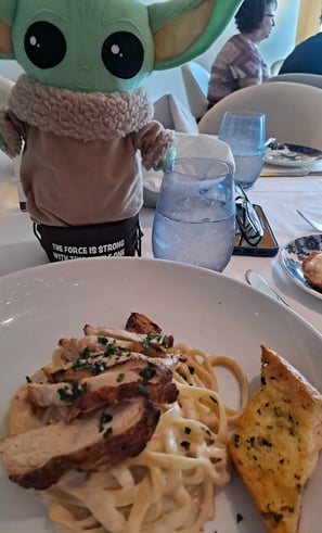 Little Green companion standing in front of a plate of chicken fettuccini alfredo