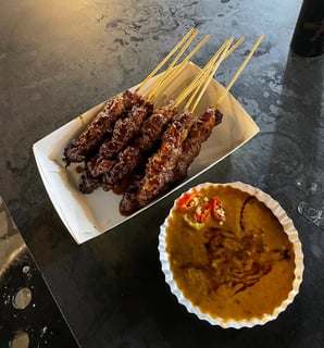 sate or chicken skewers with peanut sauce on the side with chillies in it