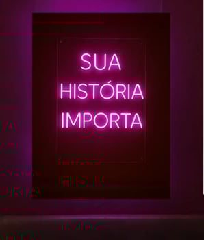 Cartaz com letras em neon na cor rosa do projeto Maria’s: Sua História Importa