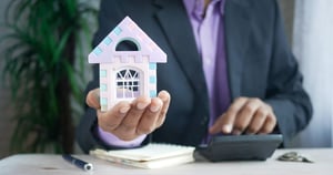 man holding a model house in his hand and calculator. Photo by Towfiqu barbhuiya on Unsplash