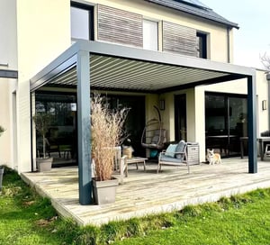 Pergola adossée en aluminium gris installée sur une terrasse moderne avec salon de jardin.