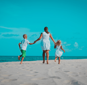 a mother and her two kids walk down the beach holding hands, their backs are to us