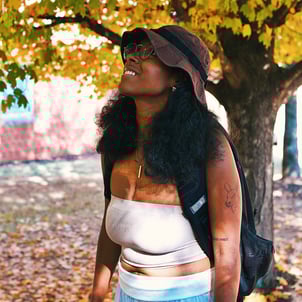 Young college black woman birdwatching underneath golden yellow autumn trees.
