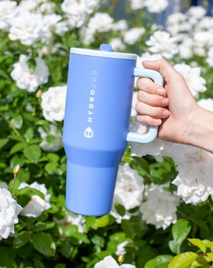 a person holding a blue coffee mug in front of a bush