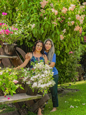 Fundadoras de Alianzas Ancestrales de pie en un jardín lleno de flores, una abrazando a la otra, reflejando unión, amor y con