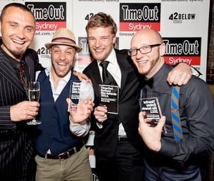 a group of men standing around celebrating winning 3 awards at an event