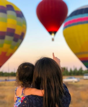 mother holding child pointing at hot air balloon symbolising hope for the future