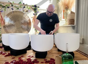 a man sitting on a wooden floor with crystal signing bowls