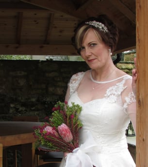 girl in an ivory vintage style wedding dress smiling with a pink floral bouquet in her hands