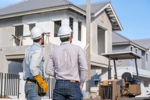 two men in hard hats standing in front of a house
