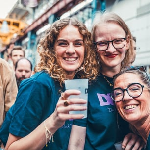 3 femmes un verre à la main au milieu de la foule
