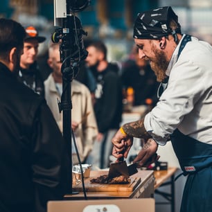 Un cuisinier en blanc avec un tablier bleu découpant de la viande sur une planche à découper