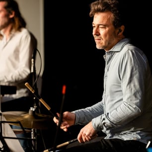 Un musicien en chemise grise jouant de la batterie