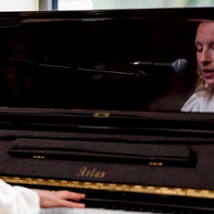 Une jeune femme jouant du piano droit et chantant dans le micro