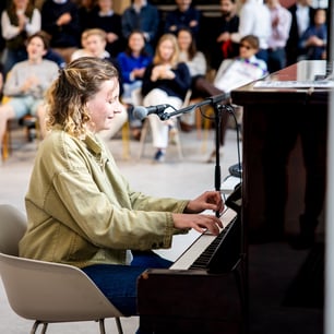Une jeune femme jouant du piano droit devant un groupe de personnes assises