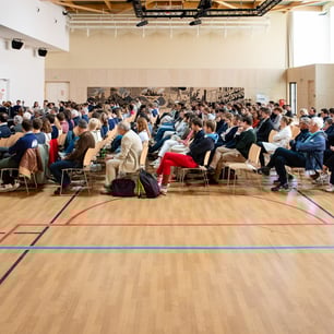 Une foule de personnes réunies et assises au milieu d'une salle de sport