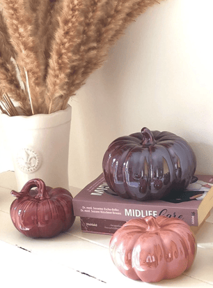 a vase with dried wheat and three purple ceramic pumpkins