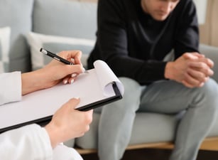 a man and woman sitting on a couch with a clipboard