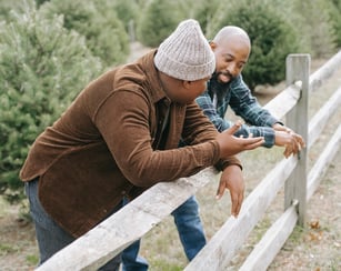 A father and son leaning with their elbows on a wooden fence having a conversation