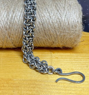 Photo of a chainmaille bracelet made of stainless steel draped over a bundle of jute twine