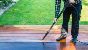 un homme nettoyant une terrasse avec un nettoyeur haute pression.