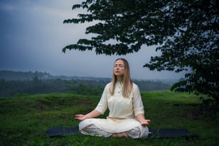 a woman sitting on a mat mat in a field doing meditation