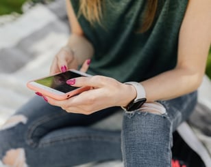 A teenage girl wearing ripped jeans sitting on a blanket looking at her phone