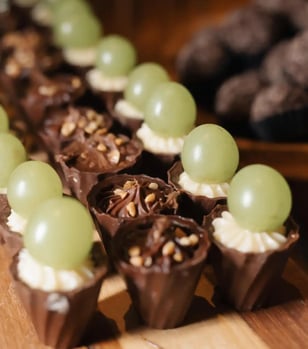 Imagem de deliciosos doces decorados com uvas verdes e cobertura de chocolate, perfeitos para festas